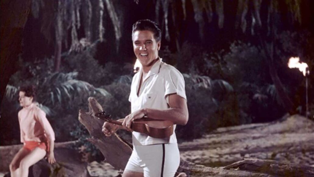 Elvis Presley smiling and holding a ukulele in a tropical nighttime setting, capturing the classic beach and music vibes you might experience at a surf camp Bali