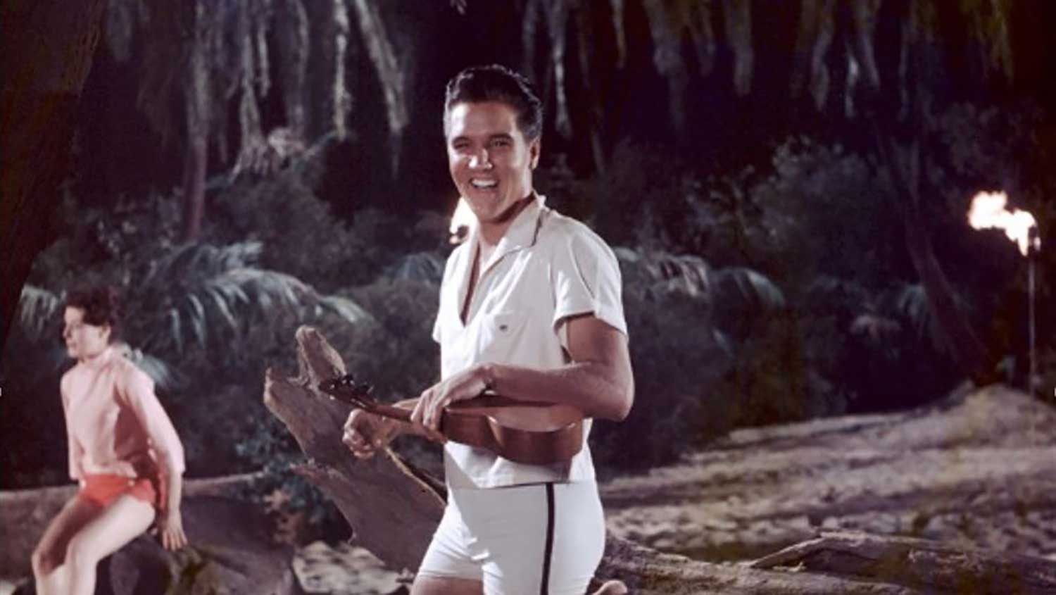 Elvis Presley smiling and holding a ukulele in a tropical nighttime setting, capturing the classic beach and music vibes you might experience at a surf camp Bali