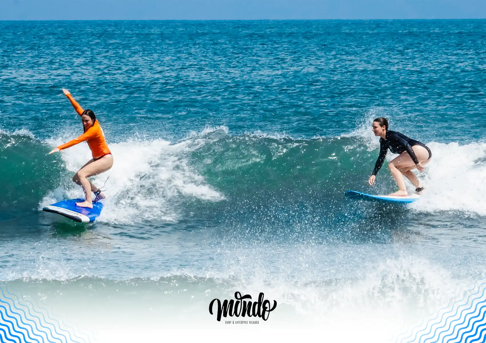 Two female surfers successfully riding waves on blue beginner boards during a lesson at a surf camp in Bali.