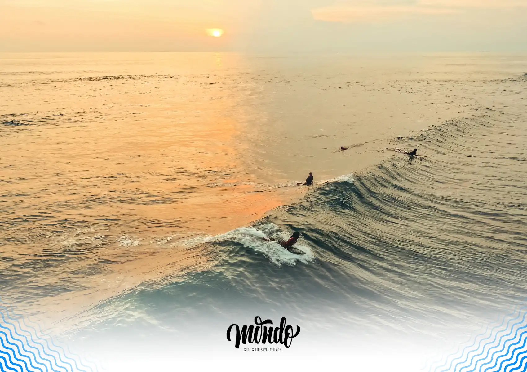 An aerial view of the ocean bathed in the golden light of sunset, where several surfers are waiting in the lineup and one gracefully catches a rolling wave, showcasing the picturesque spots accessible from a surf camp bali.