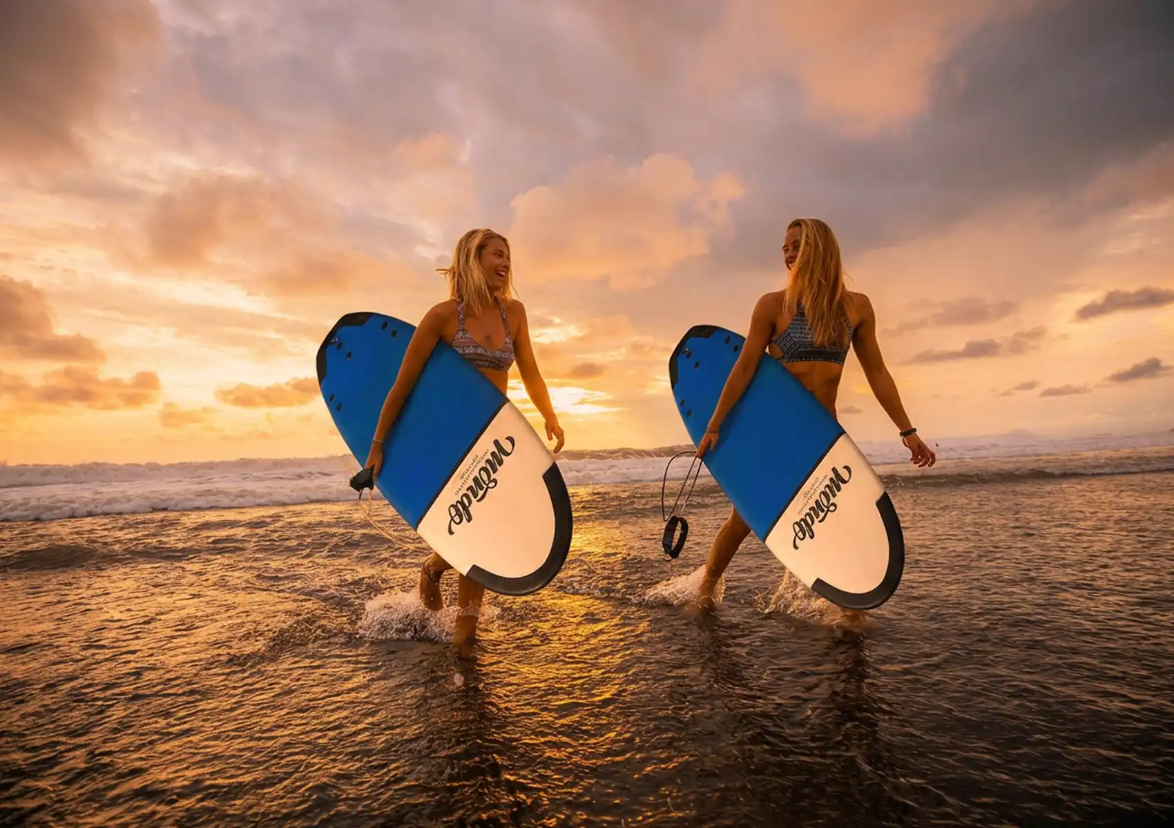 Intermediate surfers carrying different width funboards during a surf camp in Bali session focused on choosing the right surfboard dimensions.