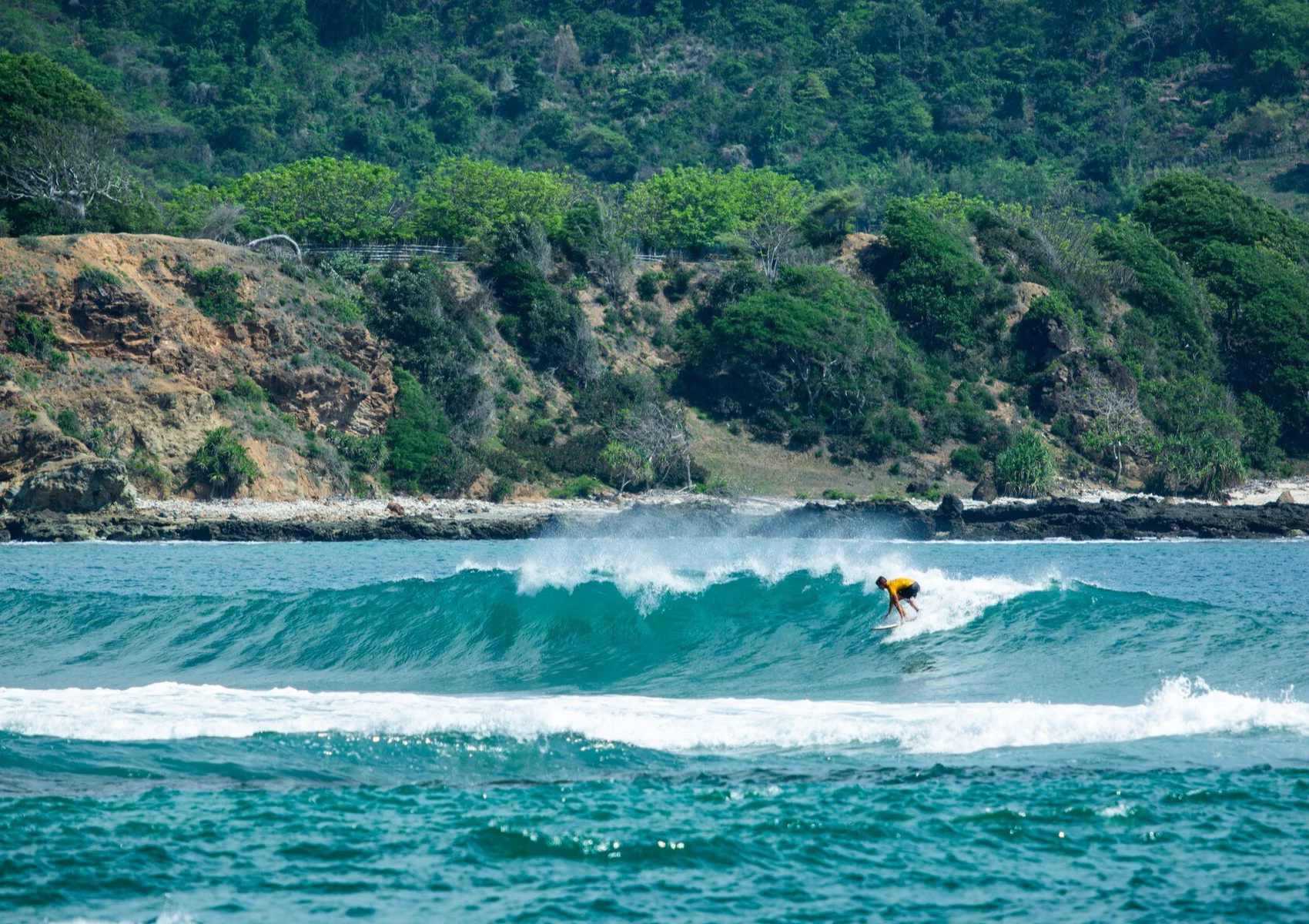 Surfer riding Bali reef break waves during the dry season at a surf camp in Bali.