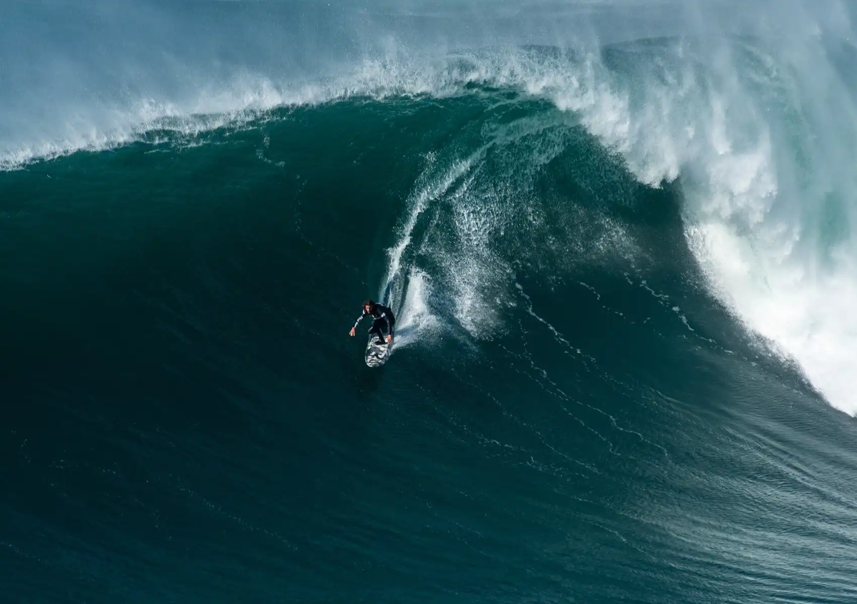 An aerial view of a surfer dropping in on a massive wave, illustrating advanced wave selection taught at a surf camp in Bali.