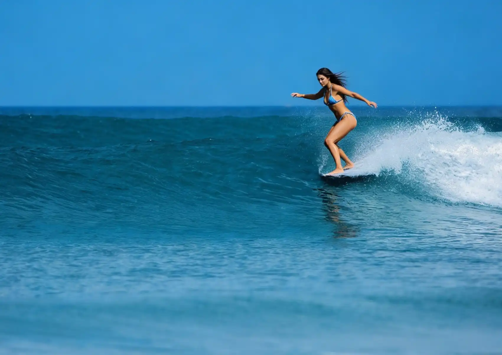 A woman in a bikini rides along the open face of a clean blue wave, demonstrating good wave selection at a surf camp in Bali.
