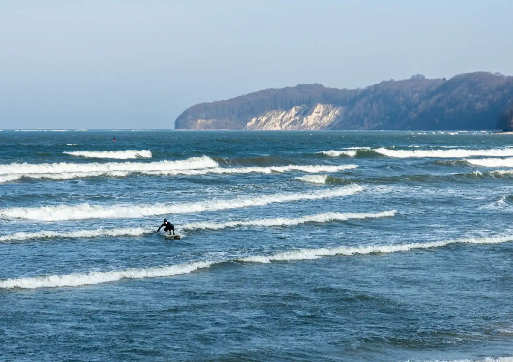 A surfer in a wetsuit rides small, choppy waves toward shore, illustrating the speed quad fins provide in weaker conditions at a surf camp in Bali.
