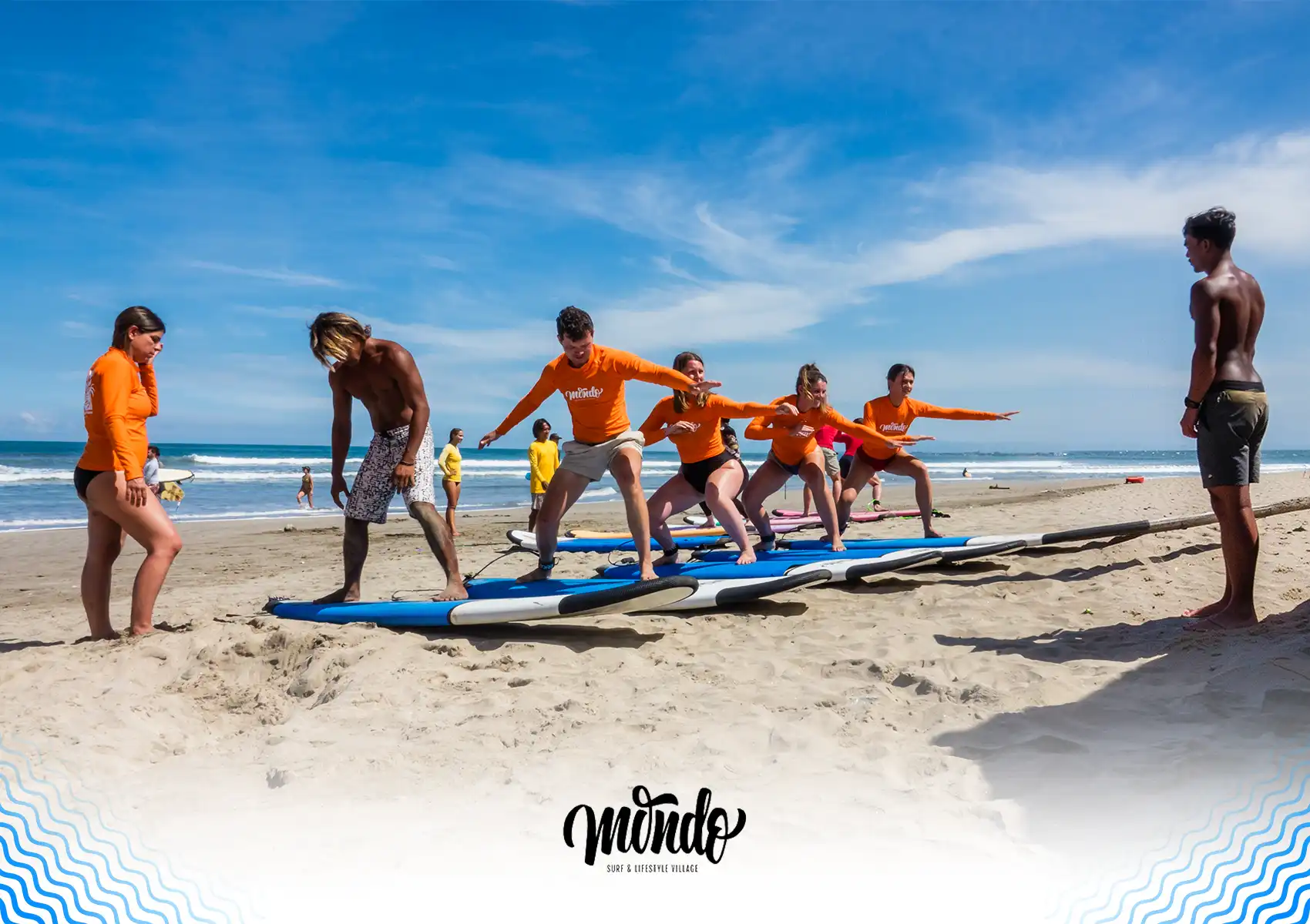 Instructors teaching a group of students how to balance and pop up on surfboards on a sandy beach at a surf camp Bali.
