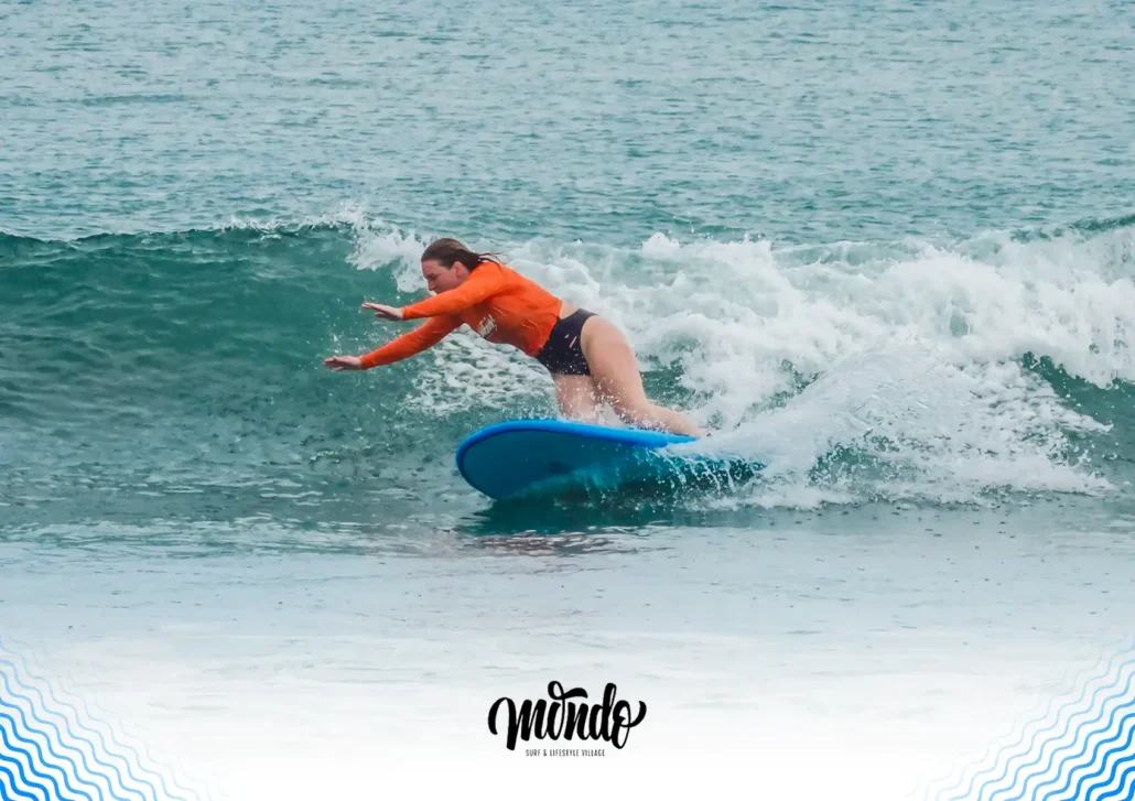 A female surfer in an orange rash guard experiencing a nosedive on her blue surfboard as she leans too far forward in the crashing wave at a surf camp bali.