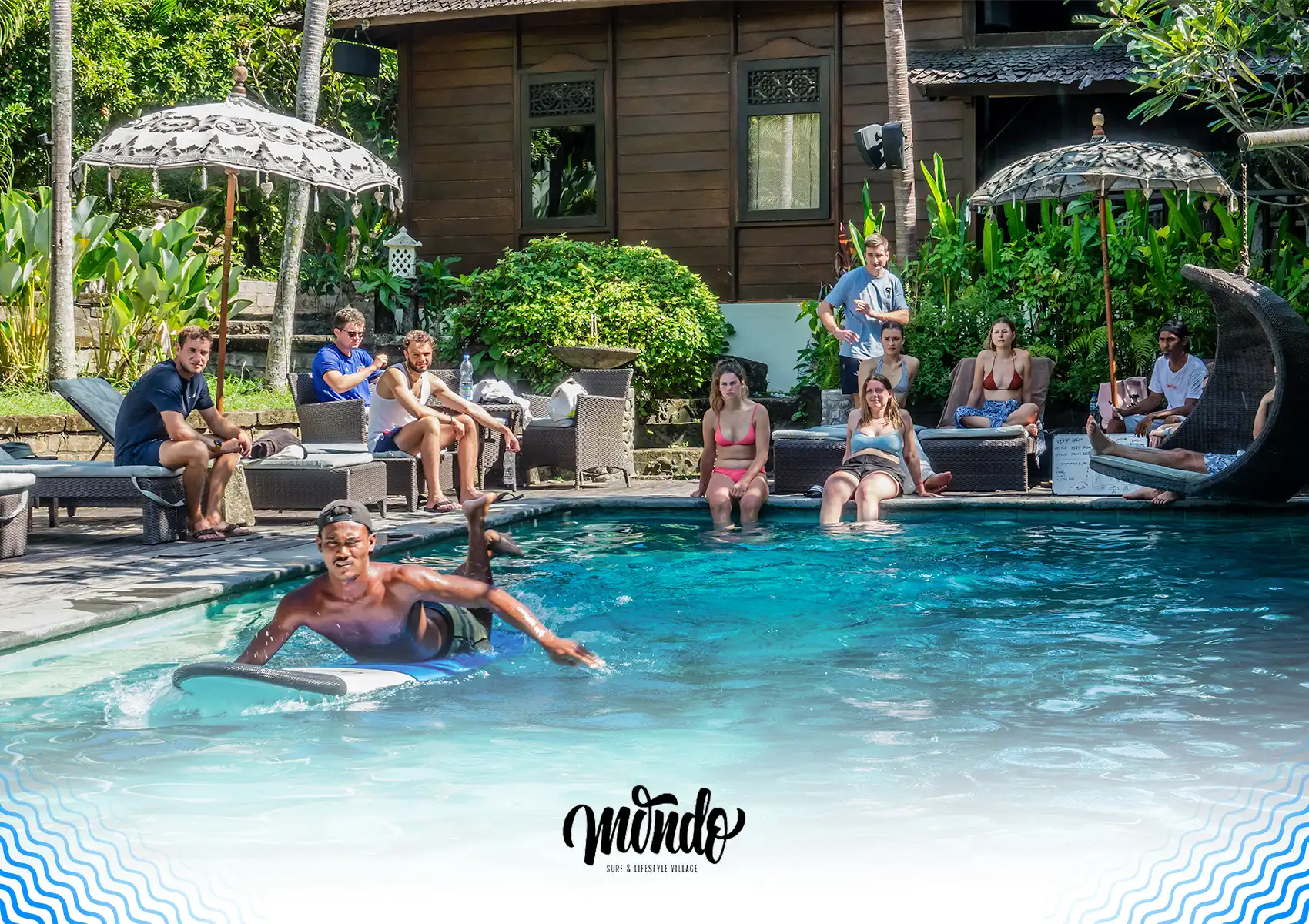 A surf instructor demonstrating paddling techniques on a surfboard in a swimming pool to a group of observing guests at a surf camp bali.