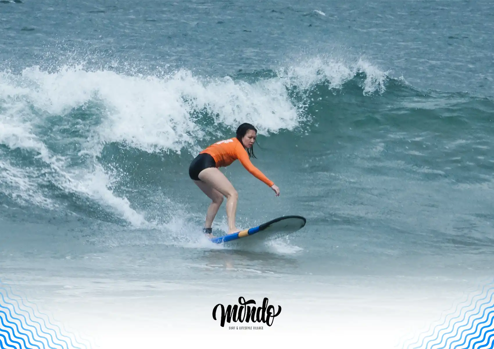 A female surfer riding a small wave on a blue soft-top board, maintaining a low, balanced stance to prevent beginner surfing mistakes.