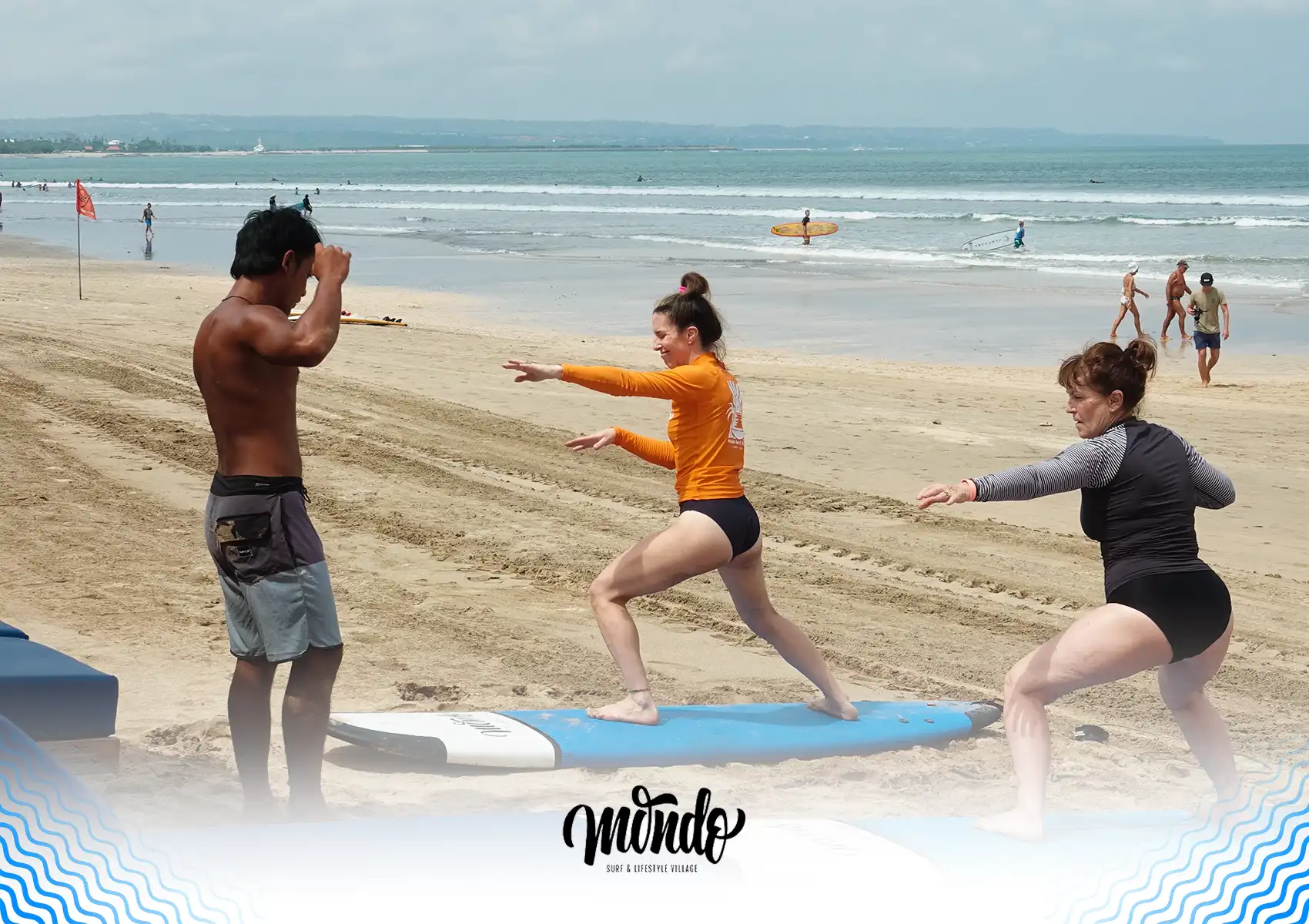 A surf instructor teaching two women the proper surfing stance as they practice popping up on their boards on the sandy beach during a lesson at a surf camp bali.