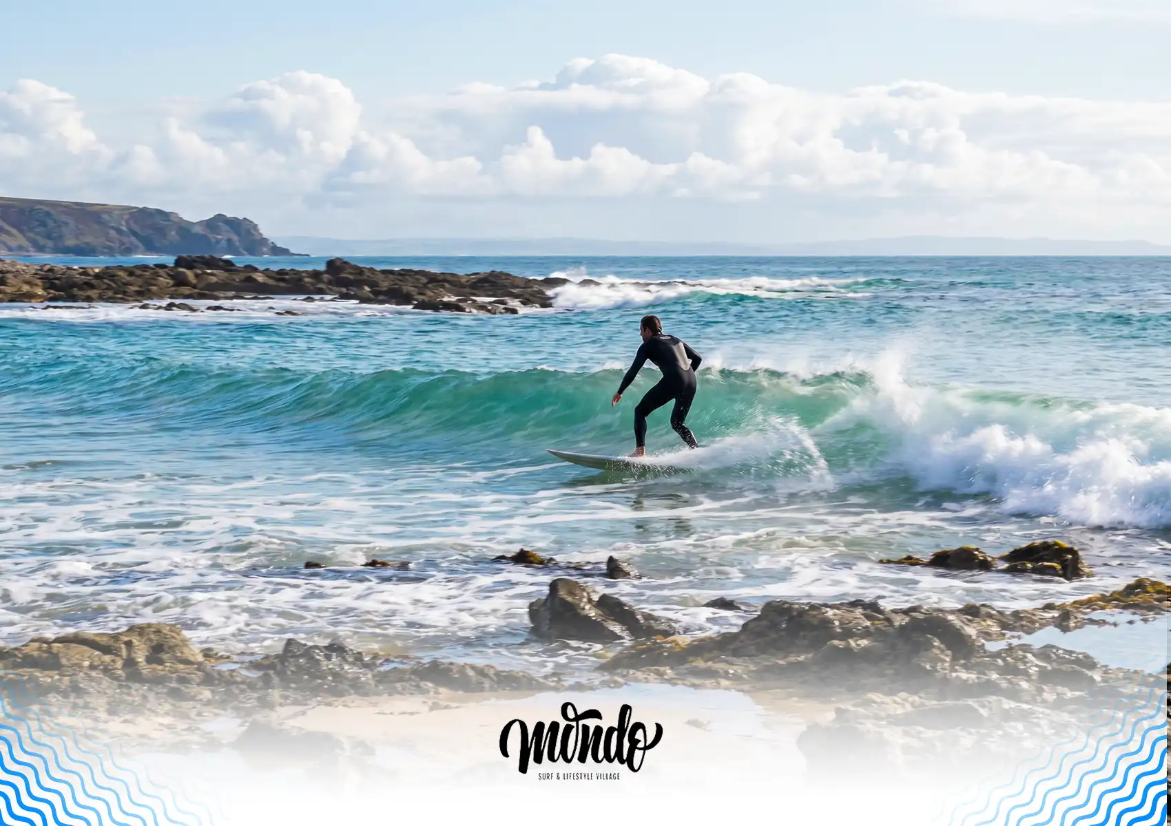 A surfer in a wetsuit riding a small wave near exposed coastal rocks and reef during low tide at a surf camp bali.