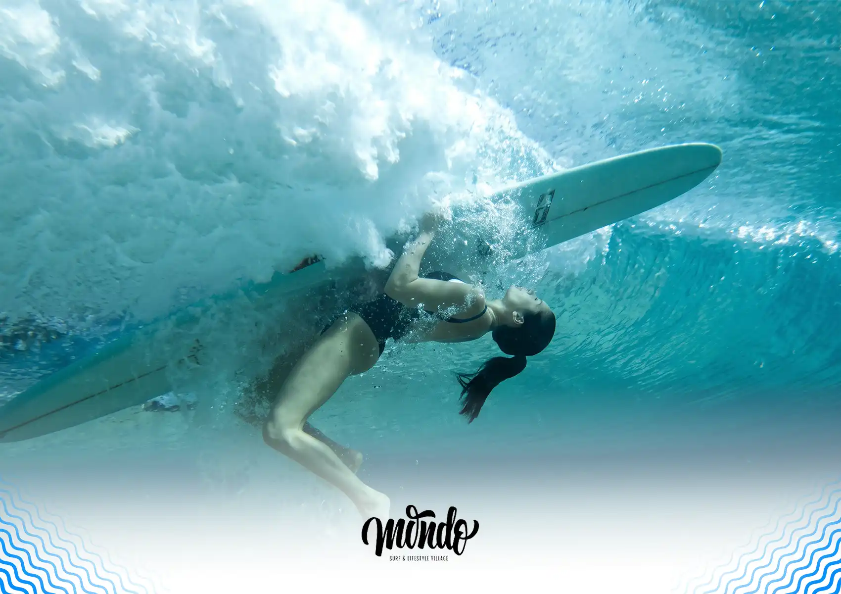 An underwater view of a female surfer performing a turtle roll, holding tightly to her surfboard as a wave crashes above her at a surf camp bali.