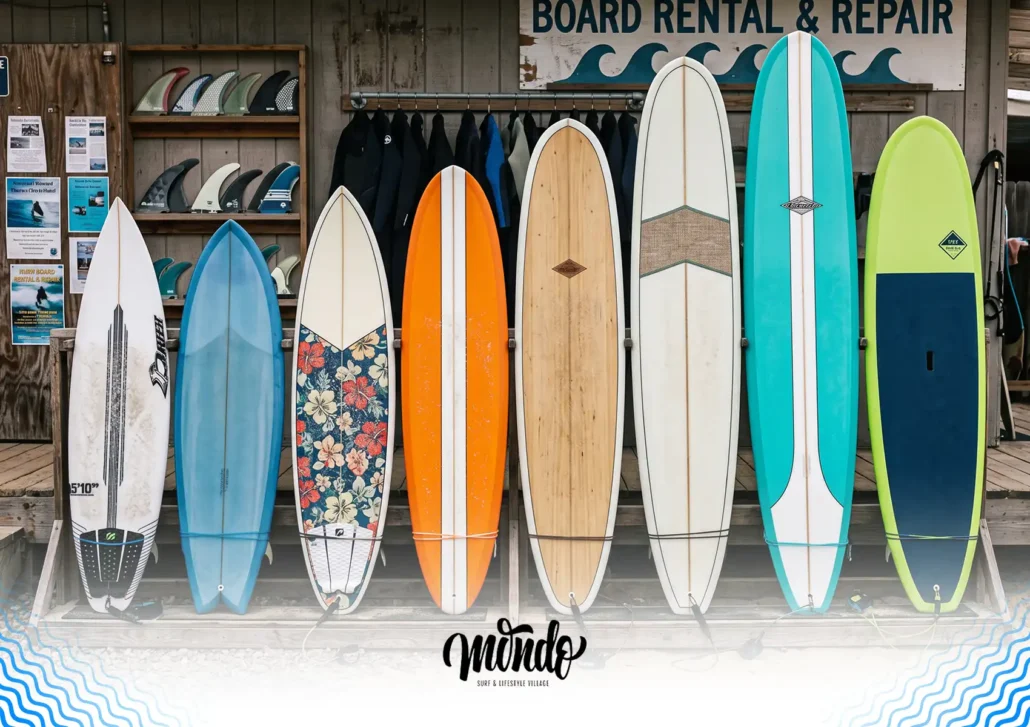 A colorful selection of different types and sizes of surfboards lined up on a rack outside a board rental and repair shop at a surf camp bali.