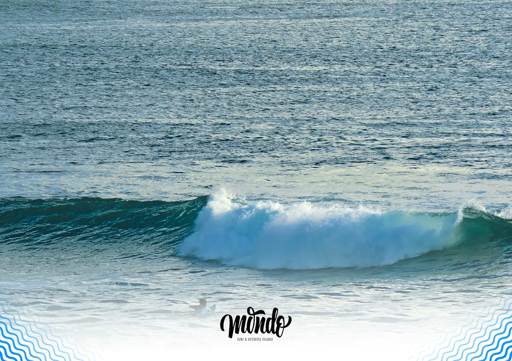 A surfer paddling out towards a surging blue wave crashing with white foam in the expansive ocean near a surf camp bali.